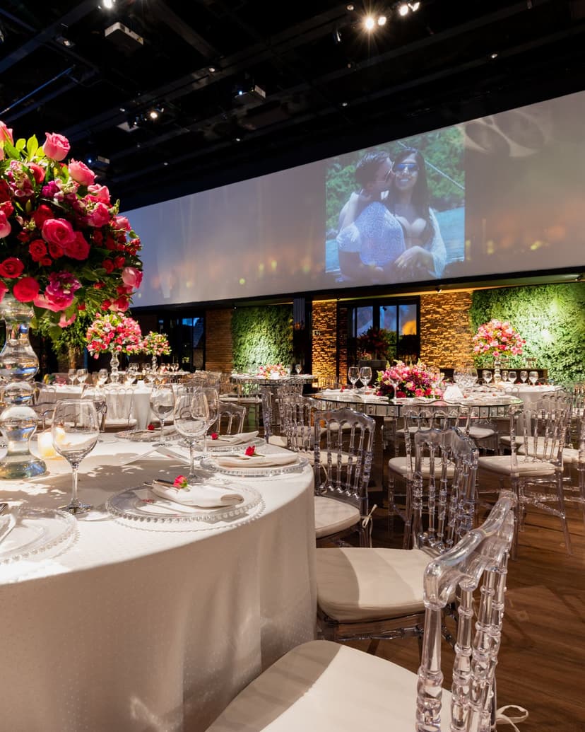 Salle de réception dressée avec tables rondes, fleurs et grands écrans